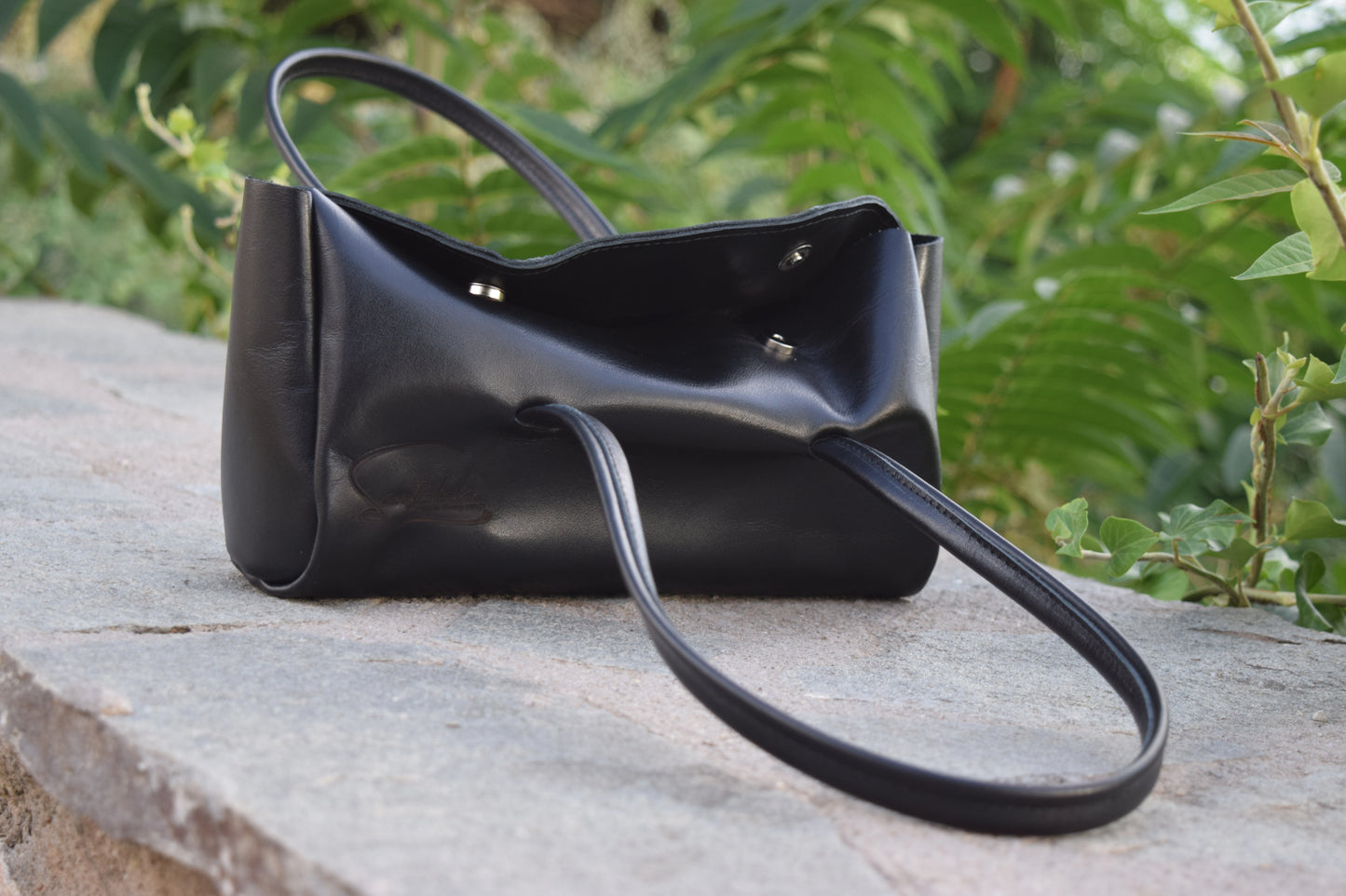 Partly open view of the Fiera Black Italian Goat Leather Handbag by Santebela, highlighting sturdy handles, silver magnetic closure, and luxurious handmade craftsmanship